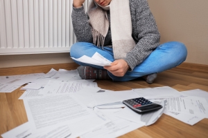 Man in A Scarf Sitting on the Floor with Utility Bills and Worried about High Heating Costs