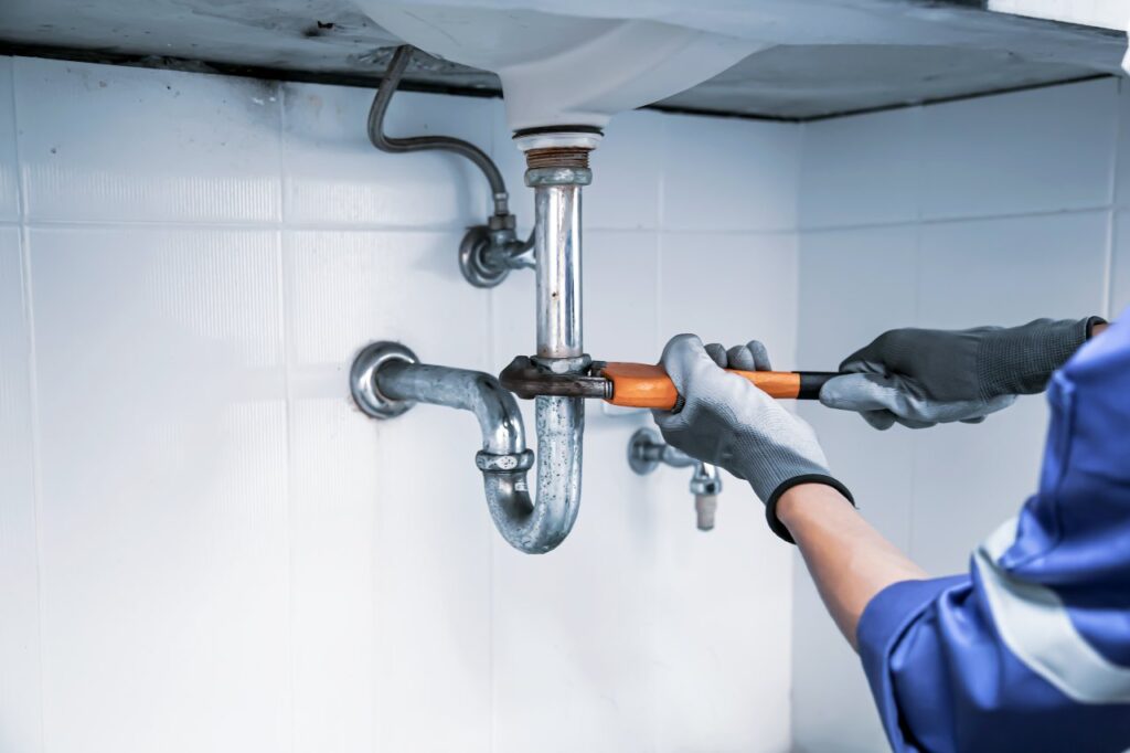 Technician plumber using a wrench to repair a water pipe under the sink. Concept of maintenance, fix water plumbing leaks, replace the kitchen sink drain, cleaning clogged pipes is dirty or rusty.